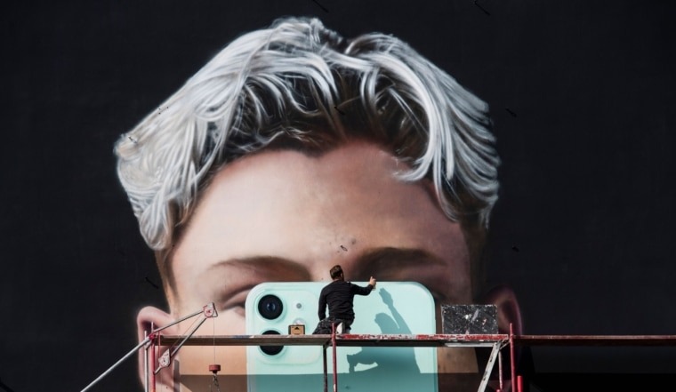 TOPSHOT - A graphic artist paints a mural ad for smartphone manufacturer Apple, in Berlin on October 1, 2020. (Photo by John MACDOUGALL / AFP) (Photo by JOHN MACDOUGALL/AFP via Getty Images)