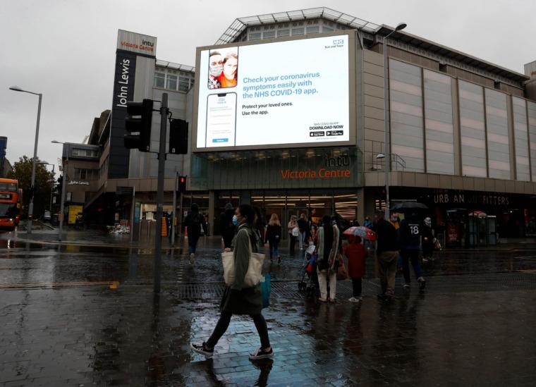 A woman wearing a face mask walks past a digital display for the NHS Covid-19 app